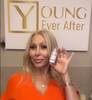 Blonde hair woman in orange dress holding bottle of plant-based Young Ever After Max Revital-Eyes Natural Rapid Firming Eye Serum
